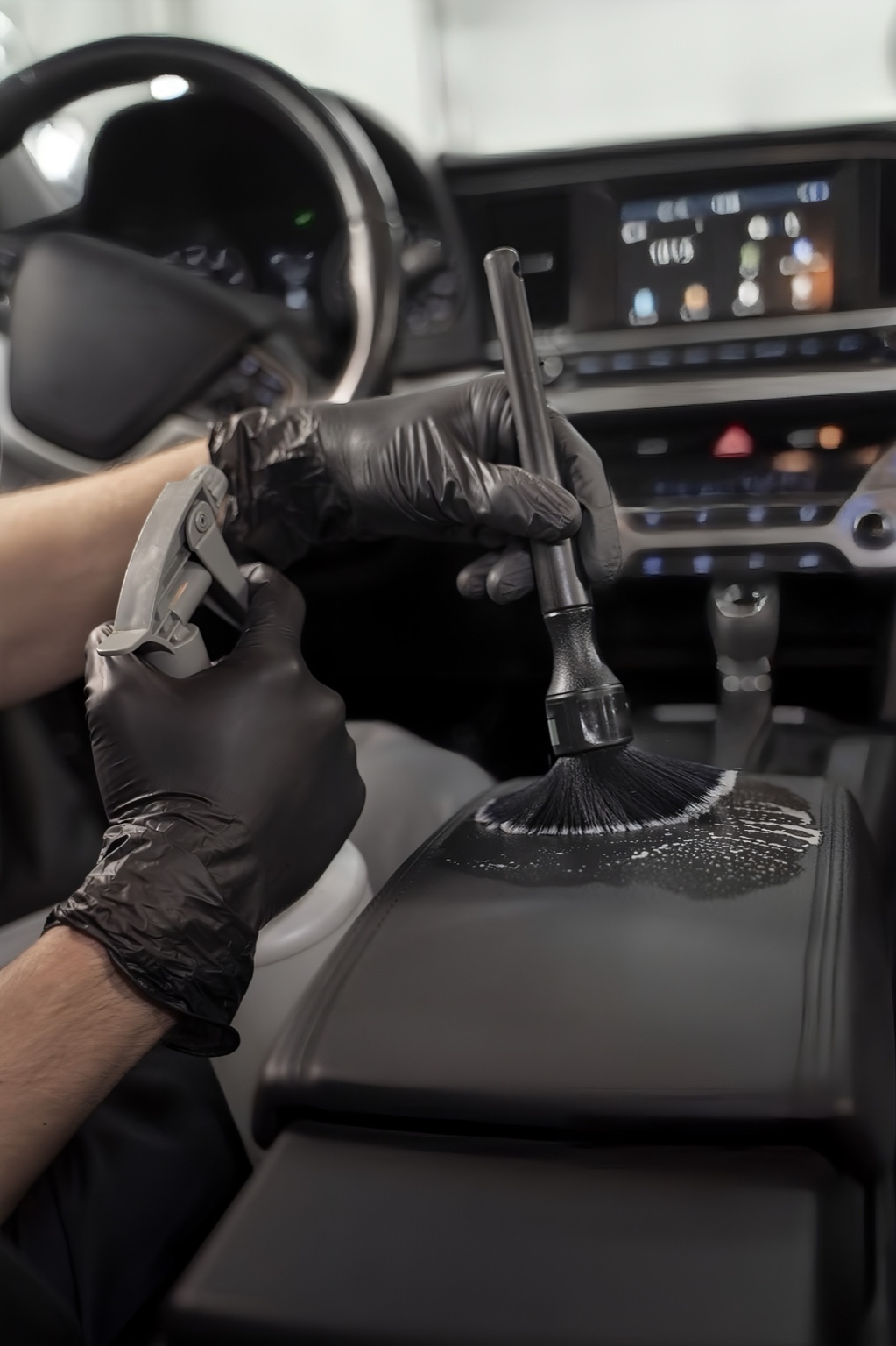 Detailer cleaning car interior with brush and spray bottle.